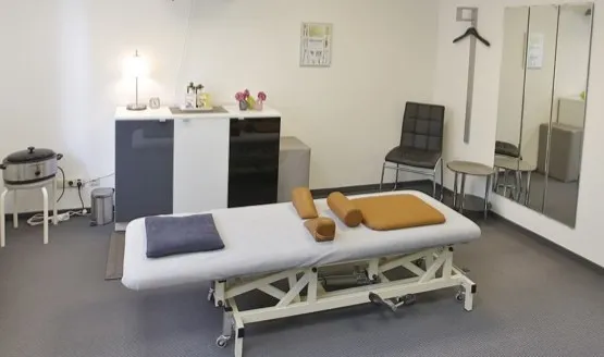 Behandlungsraum mit Liege, Spiegel und Therapiegeräten