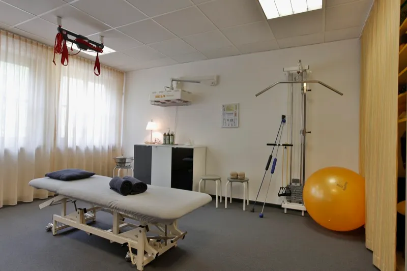 Behandlungsraum mit Liege, Gymnastikball und Therapiegeräten am Fenster