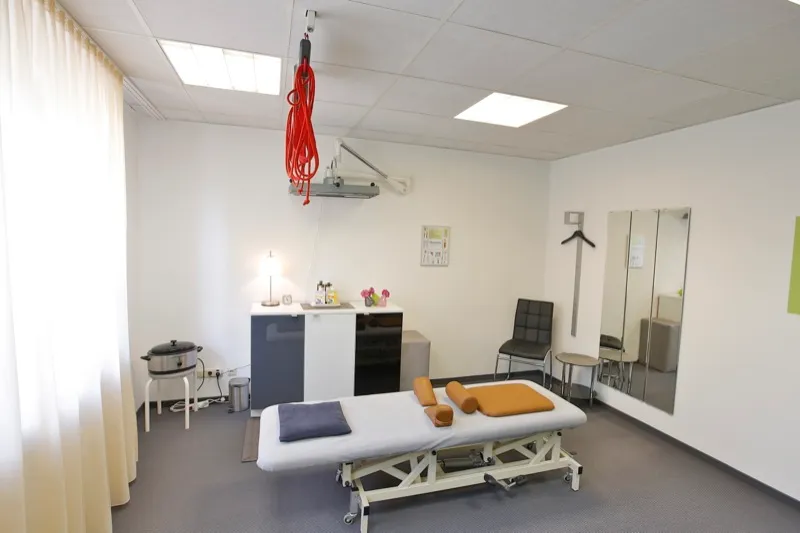Behandlungsraum mit Liege, Spiegel und rotem Schlingentisch